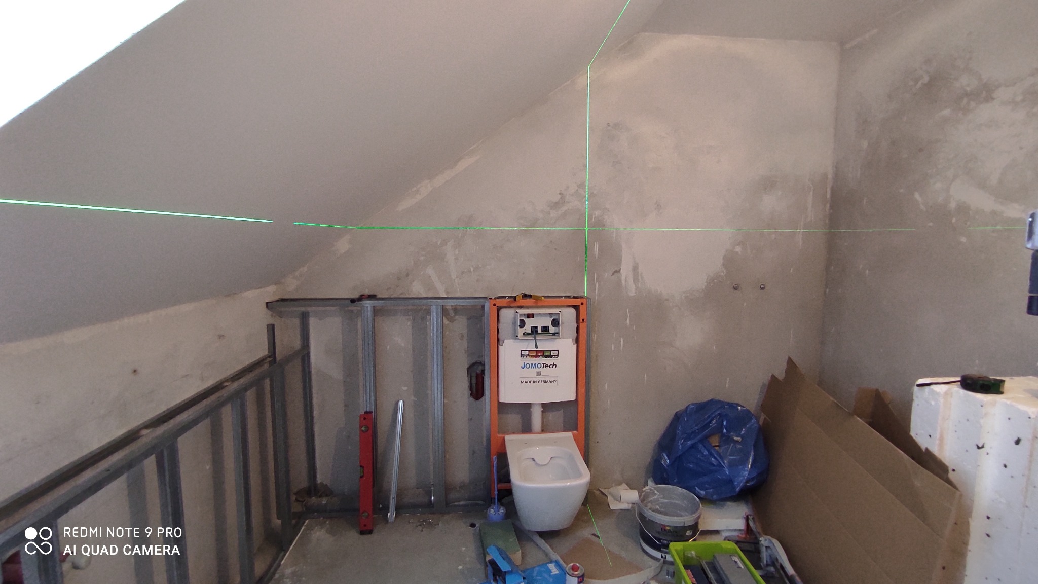 Łazienka w trakcie remontu na poddaszu ze skośnym sufitem, widoczny stelaż podtynkowy WC Jomotech, metalowa konstrukcja ścianki działowej, poziomica laserowa wyznaczająca poziom, ściany...