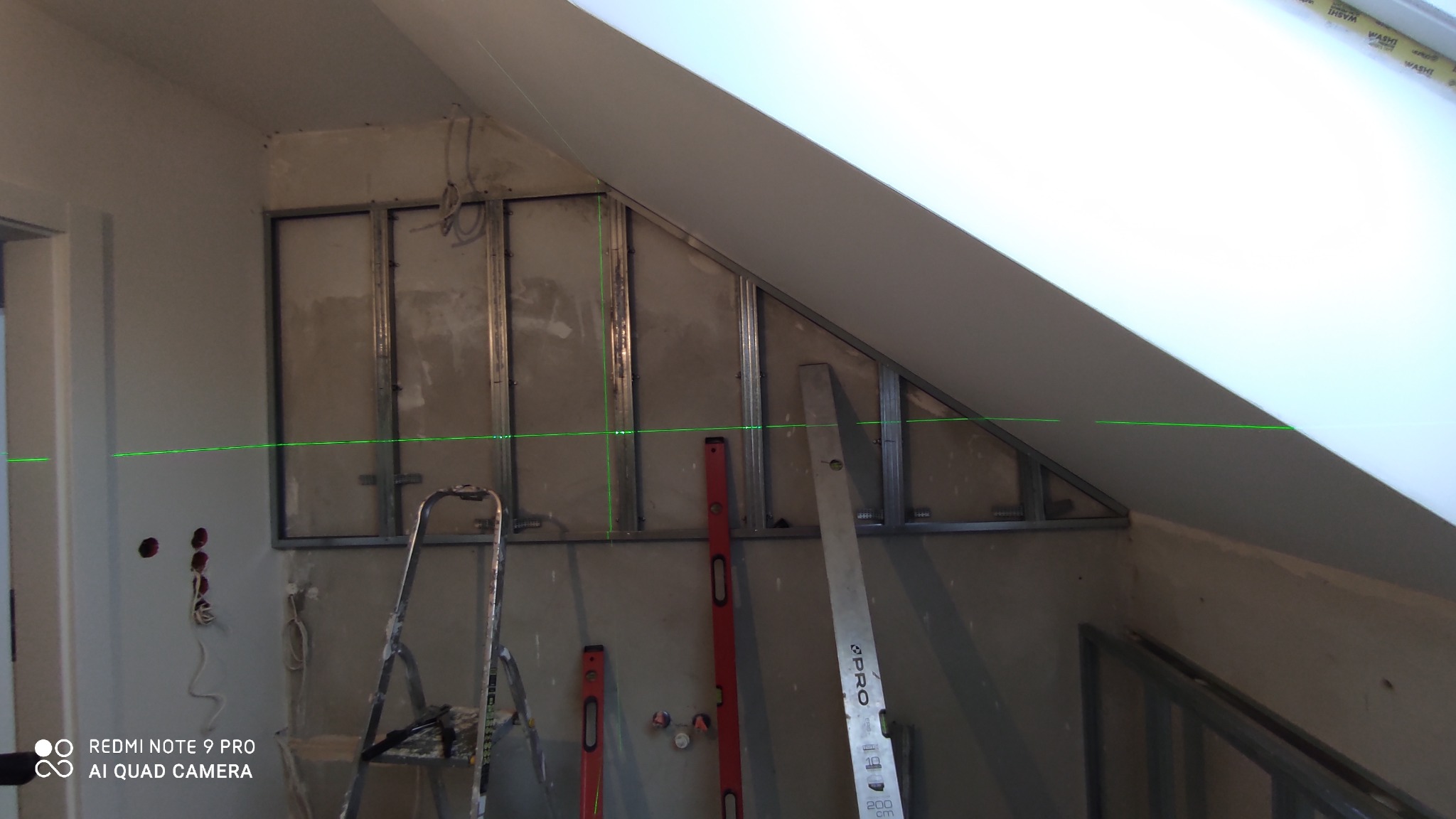 Montaż metalowego stelaża pod płytę gipsową na poddaszu, widoczne profile, poziomica laserowa i drabina.