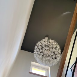 USŁUGI OGÓLNOBUDOWLANE RT - Nowoczesne wnętrze: białe ściany, czarny sufit z designerską, kulistą lampą, małe okno i drewniane elementy balustrady schodów.