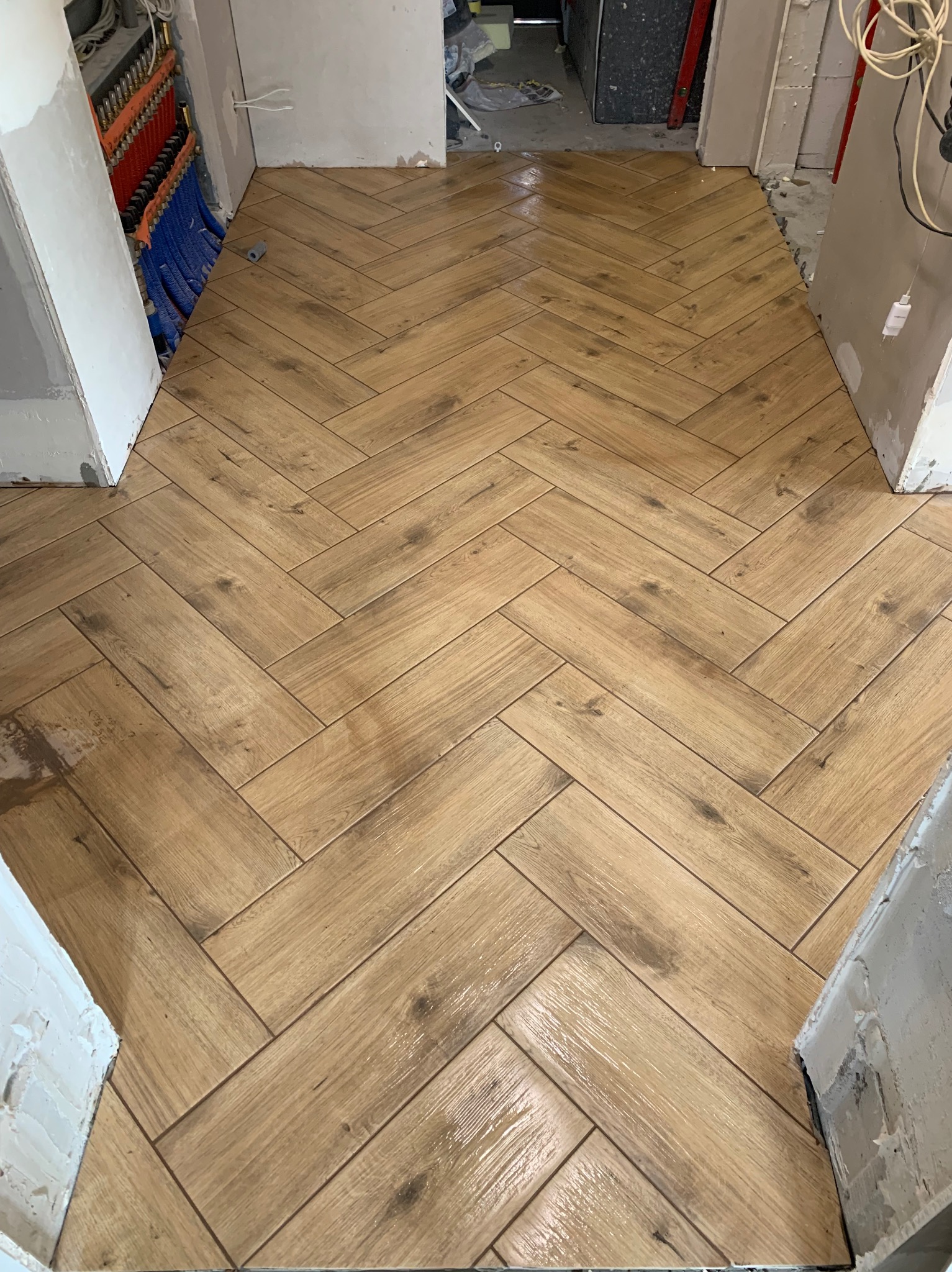 Ułożona jodełka z płytek imitujących drewno na podłodze w trakcie prac wykończeniowych, widoczne kable i instalacje w tle.