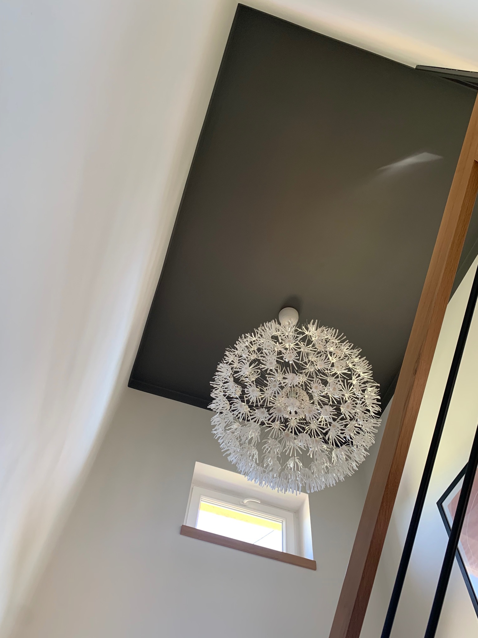 Nowoczesne wnętrze: białe ściany, czarny sufit z designerską, kulistą lampą, małe okno i drewniane elementy balustrady schodów.