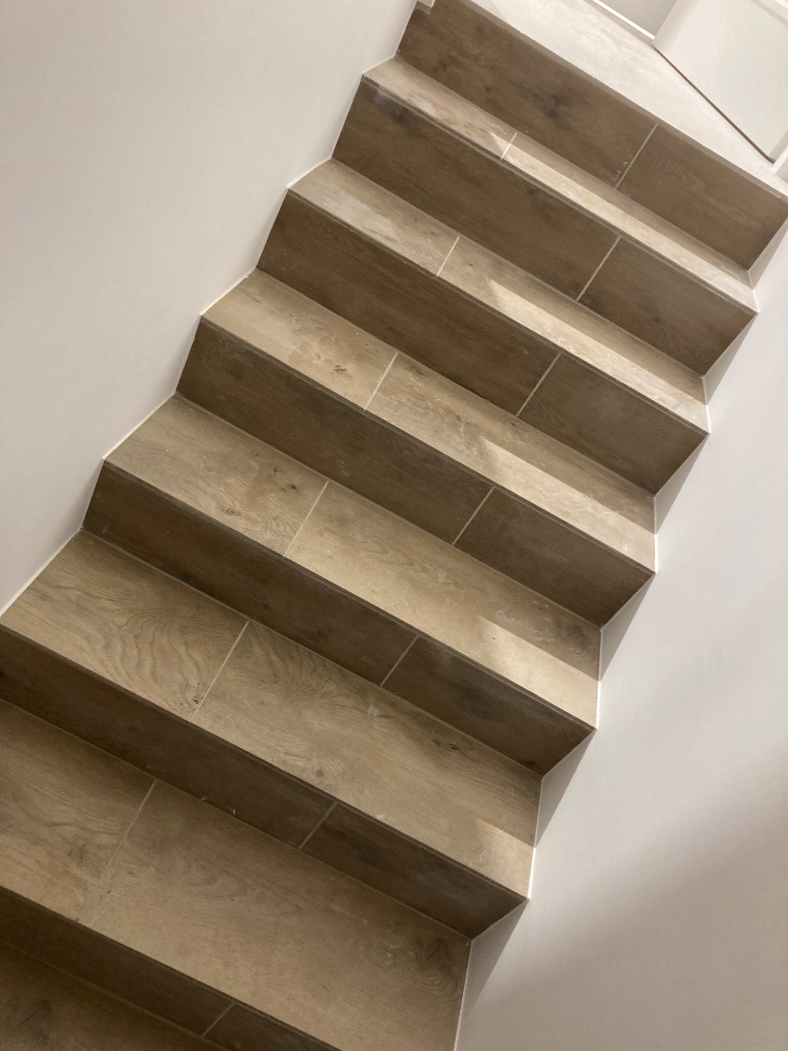 Wykończone schody wewnętrzne z płytek imitujących drewno, z widocznymi fugami i minimalistyczną białą ścianą.