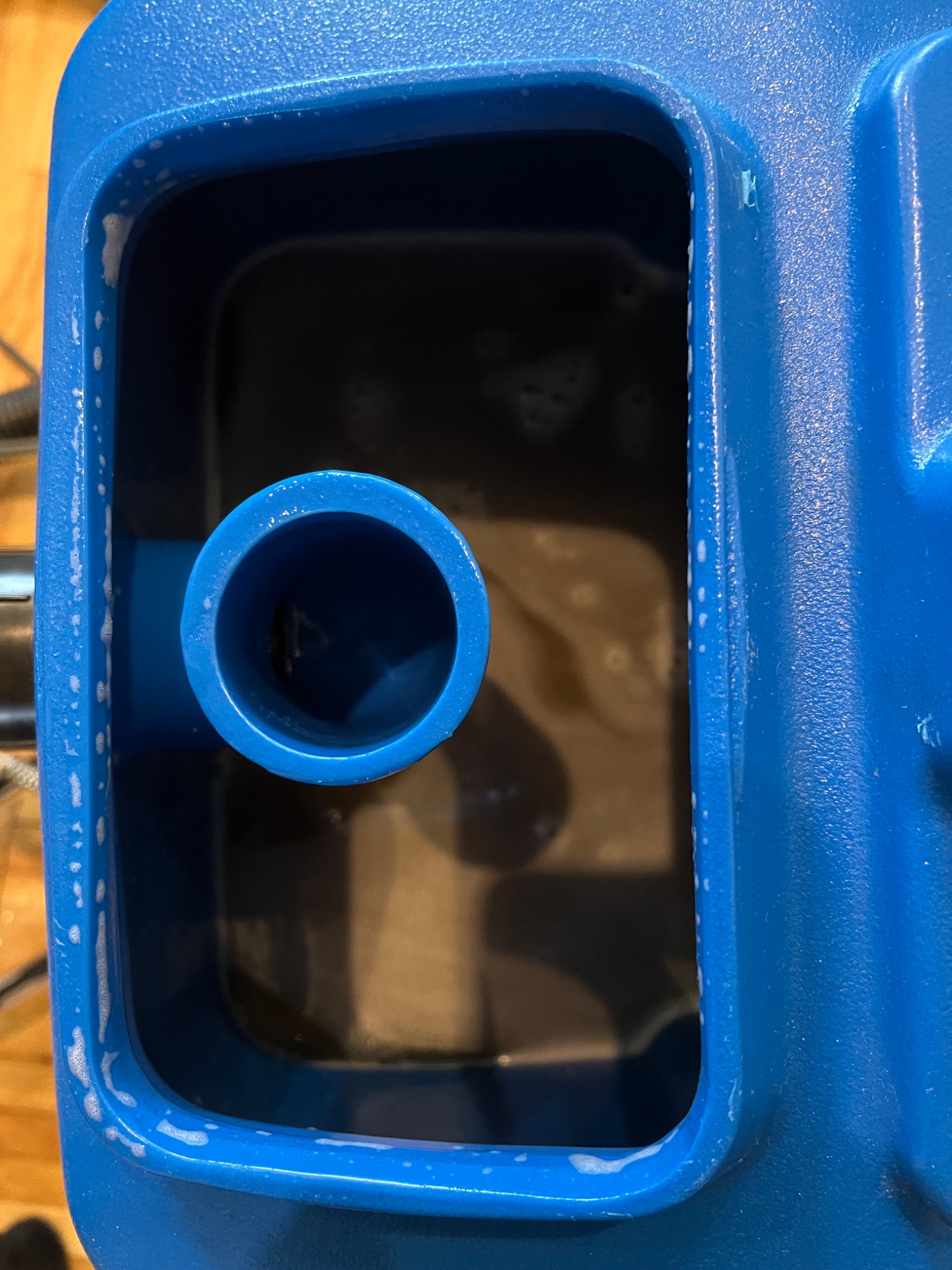 Zbiornik na brudną wodę w niebieskim odkurzaczu piorącym, widoczne resztki piany po czyszczeniu.