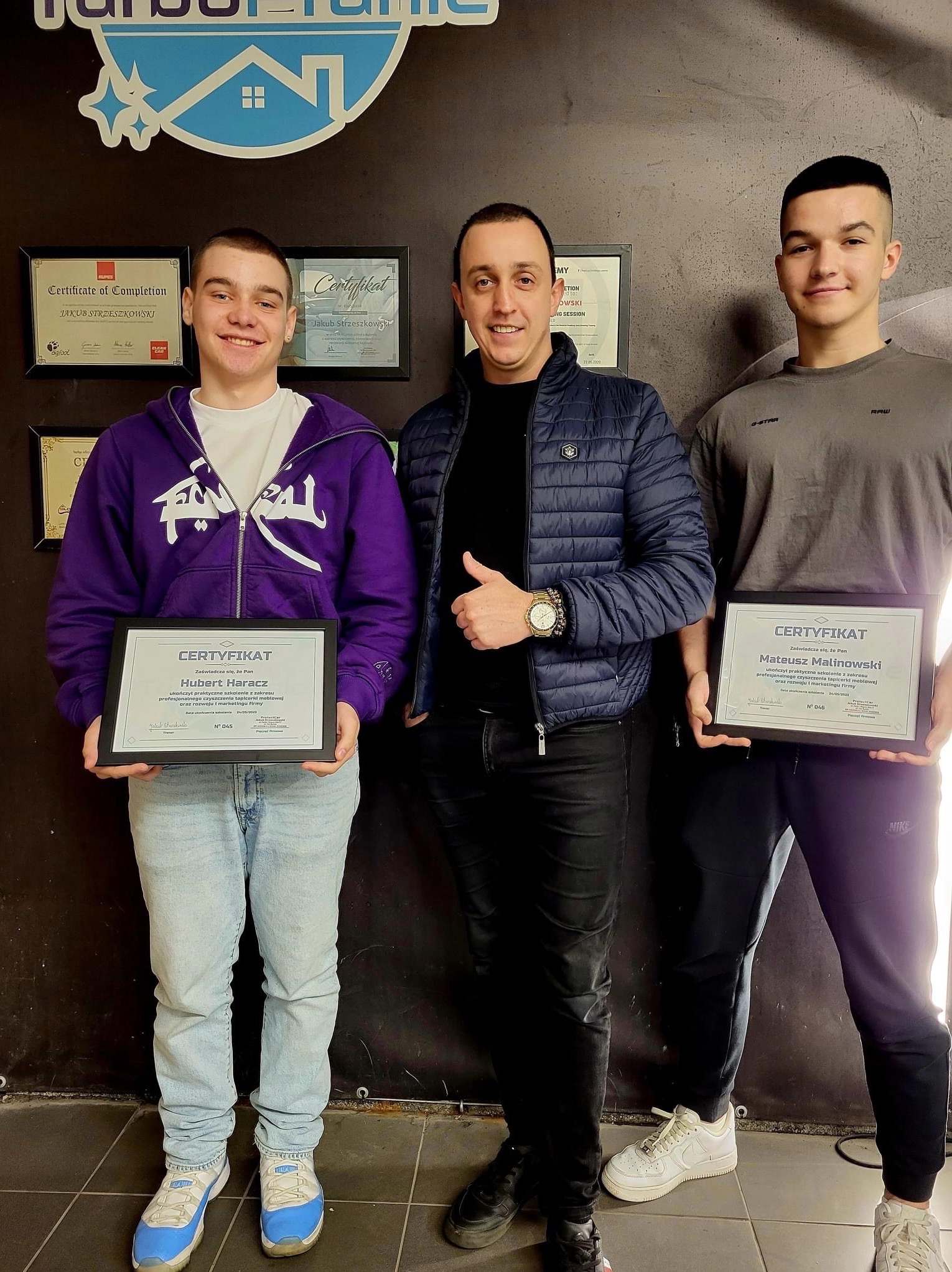 Trzech mężczyzn pozuje z certyfikatami ukończenia szkolenia z zakresu czyszczenia tapicerki meblowej, na ścianie logo firmy TurboGranie i inne certyfikaty w ramkach.