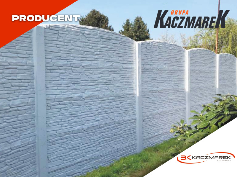 Fragment długiego, gotowego, prefabrykowanego ogrodzenia z betonu imitującego kamień, z logo producenta w rogu, na tle trawy i drzew.