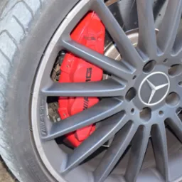 Szare felgi aluminiowe z logo Mercedes-Benz i czerwonym zaciskiem hamulcowym AMG, widoczny bieżnik opony.