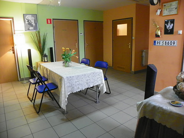 Pokój z nakrytym stołem, bukietem tulipanów, czterema krzesłami i dekoracjami ściennymi, w tym tablicą rejestracyjną.