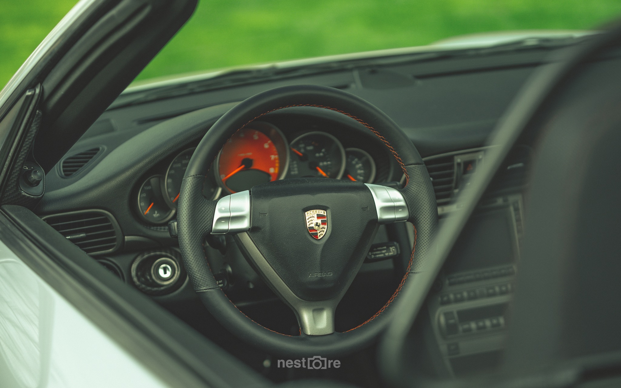 Wnętrze sportowego samochodu Porsche z widoczną deską rozdzielczą, kierownicą z logo i pomarańczowymi wskazówkami zegarów.