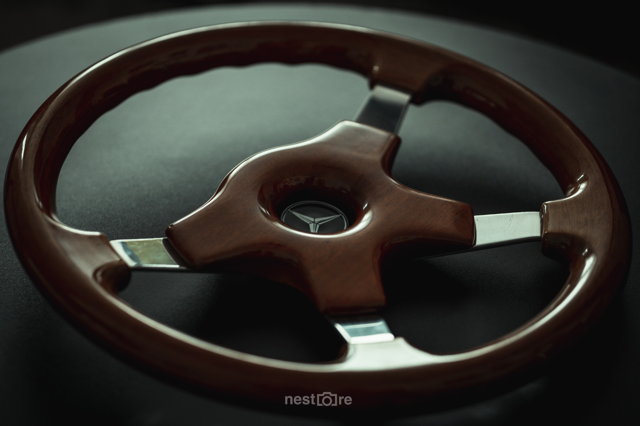 Błyszcząca, drewniana kierownica samochodowa z metalowymi elementami i logo marki na ciemnym tle.