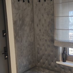 Dekor Max - Wnęka z siedziskiem i tapicerowanymi ścianami w odcieniach szarości, z haczykami na ubrania i roletą rzymską w oknie.