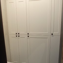 Dekor Max - Biała szafa na wymiar z ciemnymi, kwadratowymi uchwytami w łazience z wzorzystą, czarno-białą podłogą i widoczną częścią wanny.