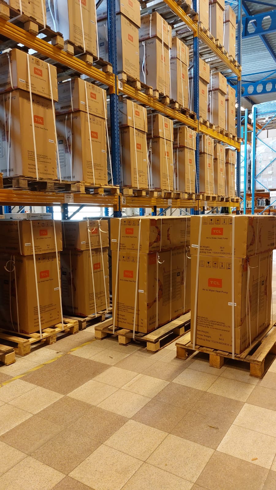 Magazyn w Chorzowie: Rzędy kartonów z urządzeniami grzewczymi marki TCL, ułożone na paletach na metalowych regałach.