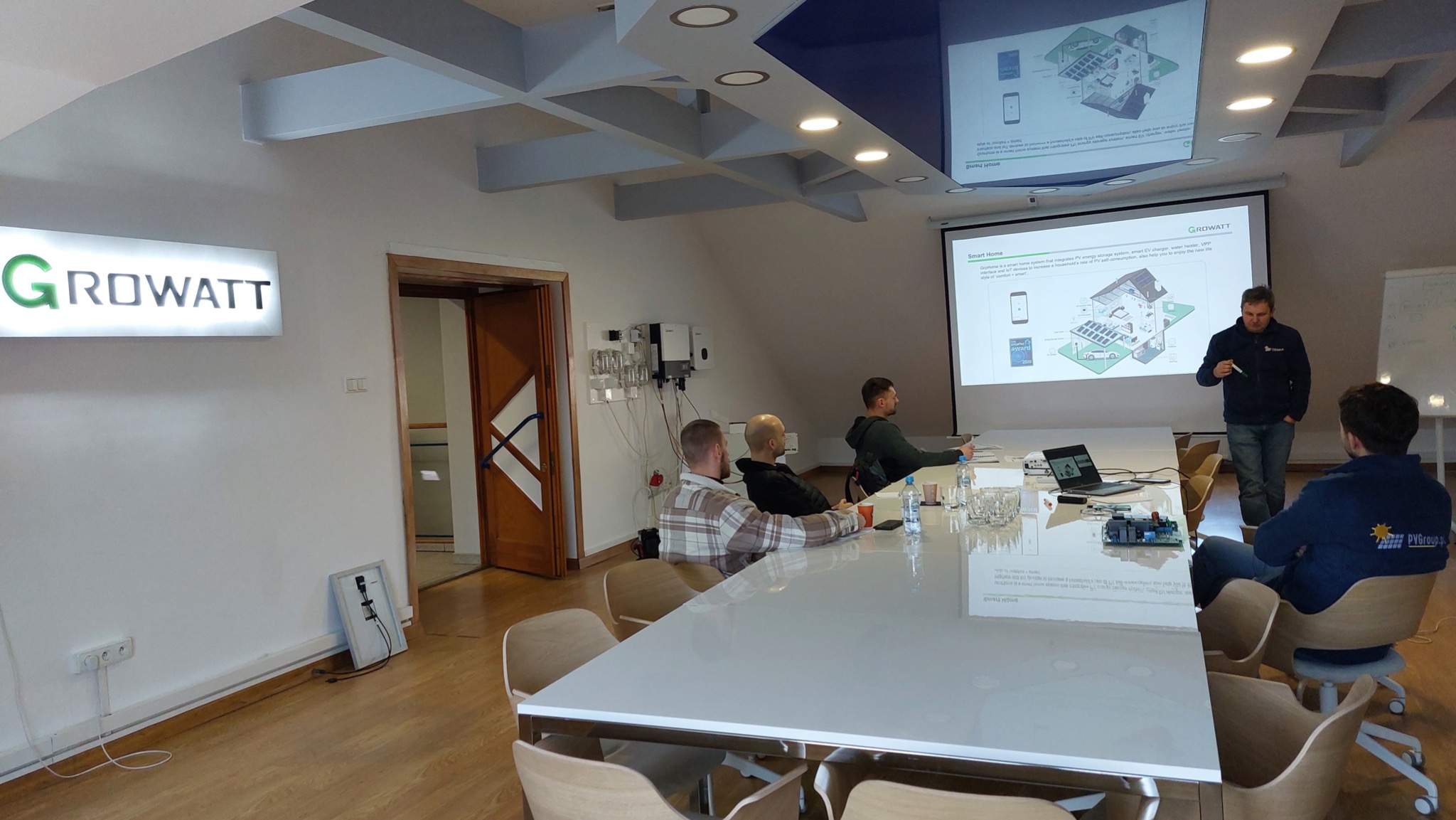 Prezentacja Growatt dotycząca inteligentnych systemów domowych z panelami fotowoltaicznymi, magazynem energii i ładowarką EV, prowadzona w sali konferencyjnej z widocznym logo firmy, inwerterami...