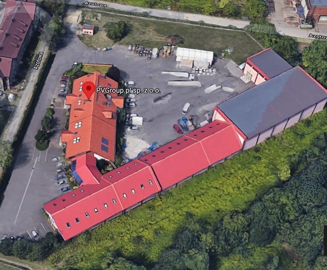 Widok z lotu ptaka na budynek firmy PVGroup.pl sp. z o.o. z czerwonym dachem, otoczony zielenią i parkingiem.
