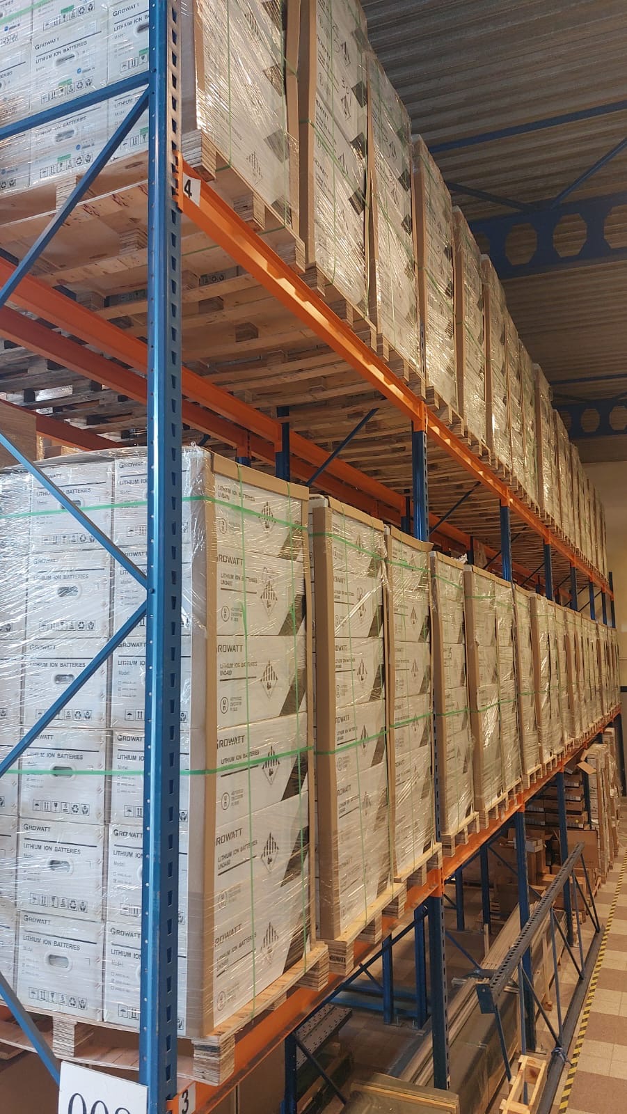 Magazyn pełen palet z opakowaniami litowo-jonowych baterii Growatt, zabezpieczonych folią, składowanych na metalowych regałach z numeracją poziomów.