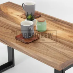 Stolik kawowy z blatem z litego drewna orzechowego, z widocznym usłojeniem, na czarnych, metalowych nogach. Na blacie dwie szare, prążkowane filiżanki na drewnianych podkładkach oraz mała roślina...