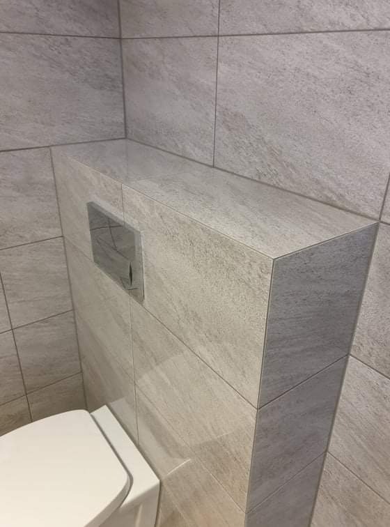 Wykończona łazienka z zabudowaną spłuczką WC, obłożona szarymi płytkami imitującymi kamień, widoczny fragment miski WC.