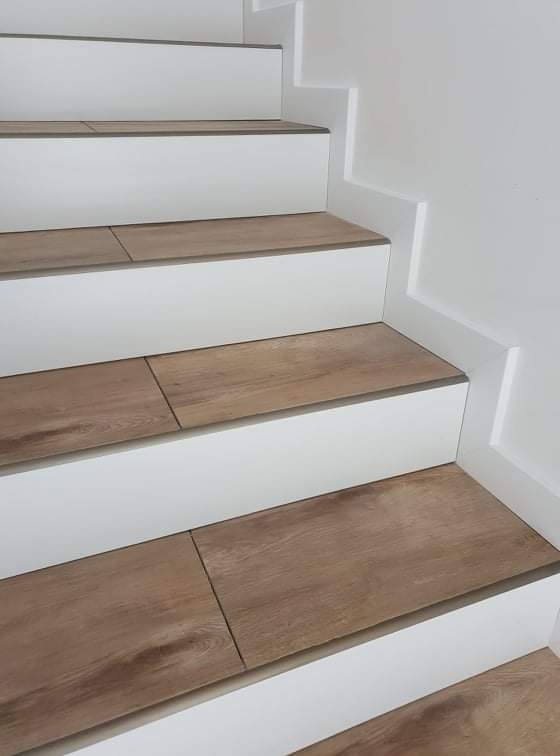 Schody z białymi podstopnicami i panelami imitującymi drewno na stopniach, wykończone szarą listwą.