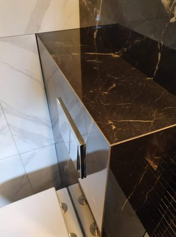 Nowoczesna łazienka z czarnym marmurowym blatem umywalki i srebrnym uchwytem szafki, kontrastująca z białymi płytkami na ścianie i podłodze.