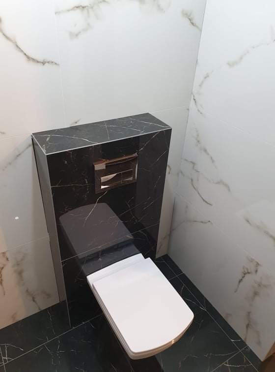 Wykończona łazienka z podwieszaną toaletą w zabudowie z czarnego marmuru z białymi żyłami, białe płytki marmurowe na ścianach i czarna marmurowa podłoga.