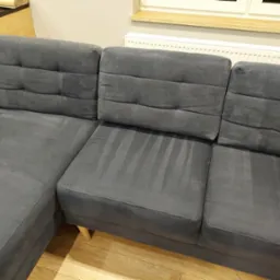 Szara, narożna kanapa z widocznymi śladami po czyszczeniu tapicerki, ukazującymi różnicę w odcieniu.