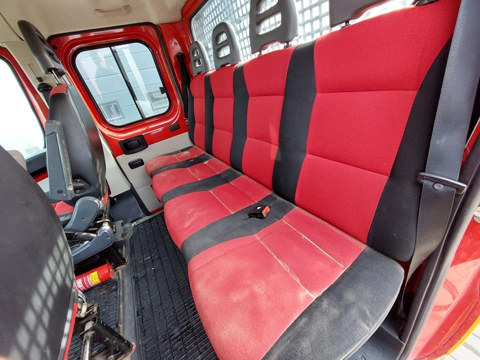 Wnętrze czerwonego samochodu dostawczego z wyraźnie zabrudzoną, czerwoną i czarną tapicerką na tylnej kanapie, widoczna gaśnica pod siedzeniem.