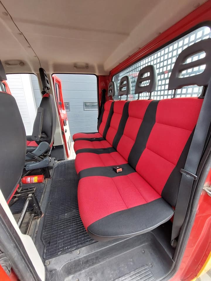 Czerwono-czarna tapicerka samochodowa w pojeździe dostawczym, widoczny gaśnica i kratka za siedzeniami.