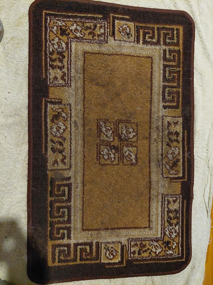 Prostokątny, brązowo-beżowy dywanik z geometrycznym wzorem na kremowym ręczniku, widoczne ślady użytkowania.