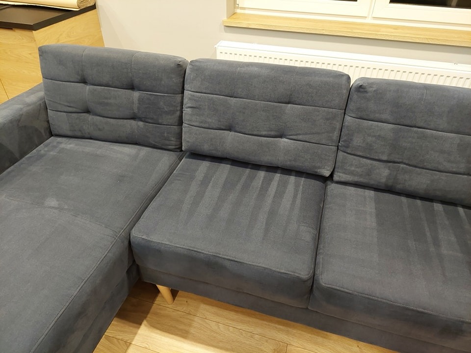 Szara, narożna kanapa z widocznymi śladami po czyszczeniu tapicerki, ukazującymi różnicę w odcieniu.