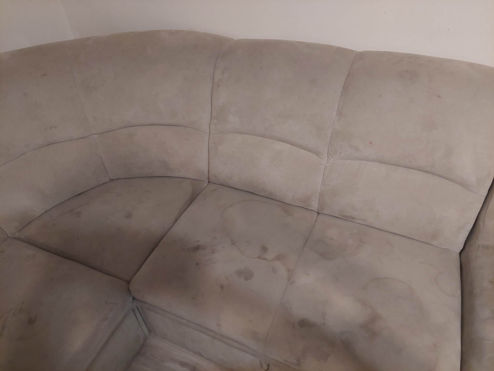 Fragment beżowej, tapicerowanej sofy z widocznymi plamami i zabrudzeniami na siedzisku i oparciu.