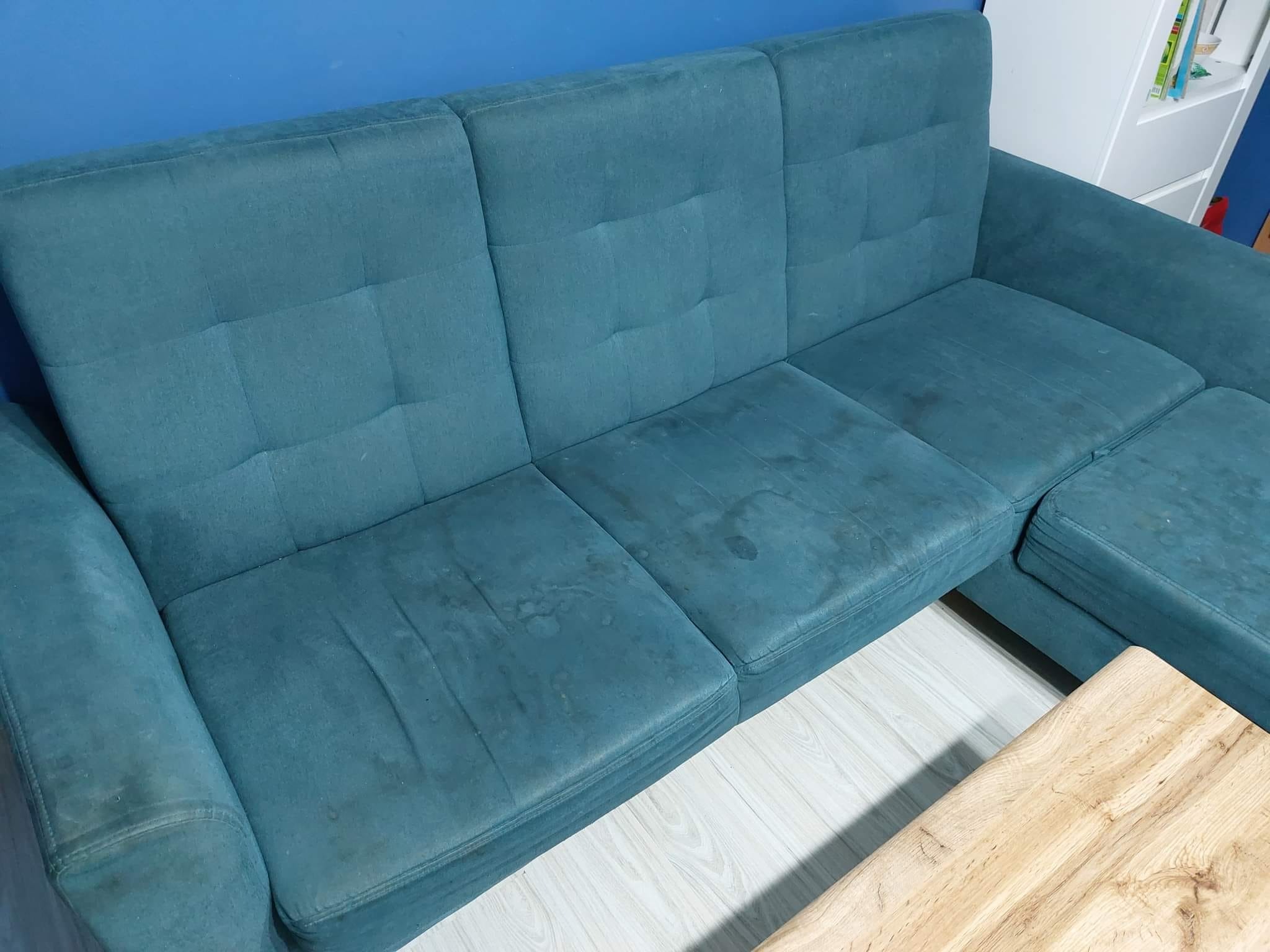 Turkusowa sofa narożna z widocznymi plamami na siedzisku, ustawiona na jasnej podłodze, z fragmentem drewnianego stolika kawowego w kadrze.