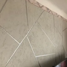 Teksturowana ściana w odcieniach beżu z geometrycznymi, srebrnymi wstawkami, wykończona dekoracyjnym paskiem pod sufitem.