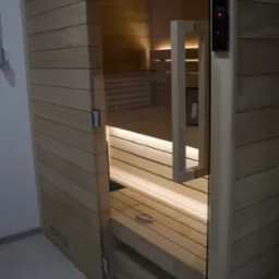 Wykończona drewniana kabina z przeszklonymi drzwiami, widoczne estetyczne docięcia pod kątem 45 stopni, schowane zawiasy w boazerii, nawiercone otwory wentylacyjne, panel sterowania na zewnątrz...