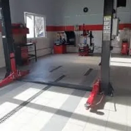 Wnętrze warsztatu samochodowego w Jankach z podnośnikiem dwukolumnowym i stanowiskiem do diagnostyki, widoczne narzędzia i wyposażenie. Jasne oświetlenie i czysta posadzka.