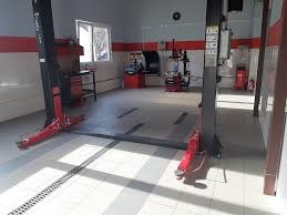 Wnętrze warsztatu samochodowego w Jankach z podnośnikiem dwukolumnowym i stanowiskiem do diagnostyki, widoczne narzędzia i wyposażenie. Jasne oświetlenie i czysta posadzka.