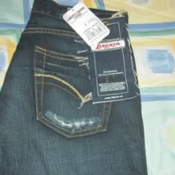 Para jeansów marki Liberto Denim z metkami, prezentujących styl vintage z przetarciami na tylnej kieszeni, leżących na wzorzystej tkaninie.