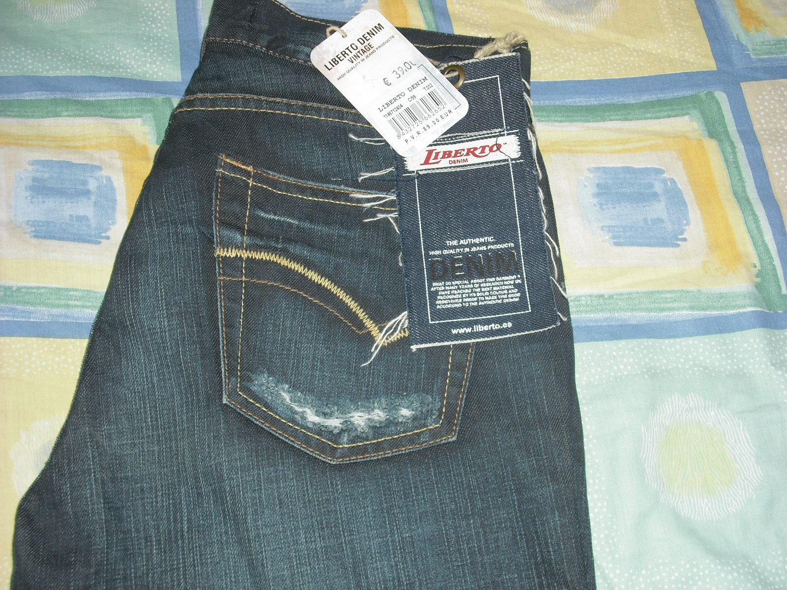 Para jeansów marki Liberto Denim z metkami, prezentujących styl vintage z przetarciami na tylnej kieszeni, leżących na wzorzystej tkaninie.