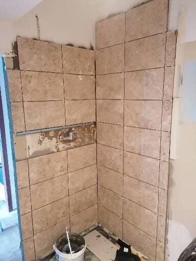 Montaż beżowych płytek w rogu łazienki w Radomiu, widoczny częściowo wykończony fragment ściany z narzędziem do nakładania kleju oraz wiadro z zaprawą.