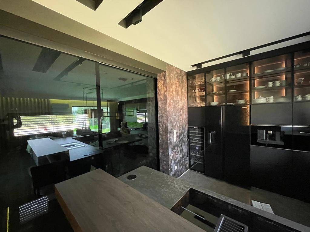 Nowoczesna kuchnia z czarnymi szafkami podświetlanymi od wewnątrz, widoczna wyspa kuchenna z drewnianym blatem i duże przeszklone drzwi przesuwne z widokiem na salon.