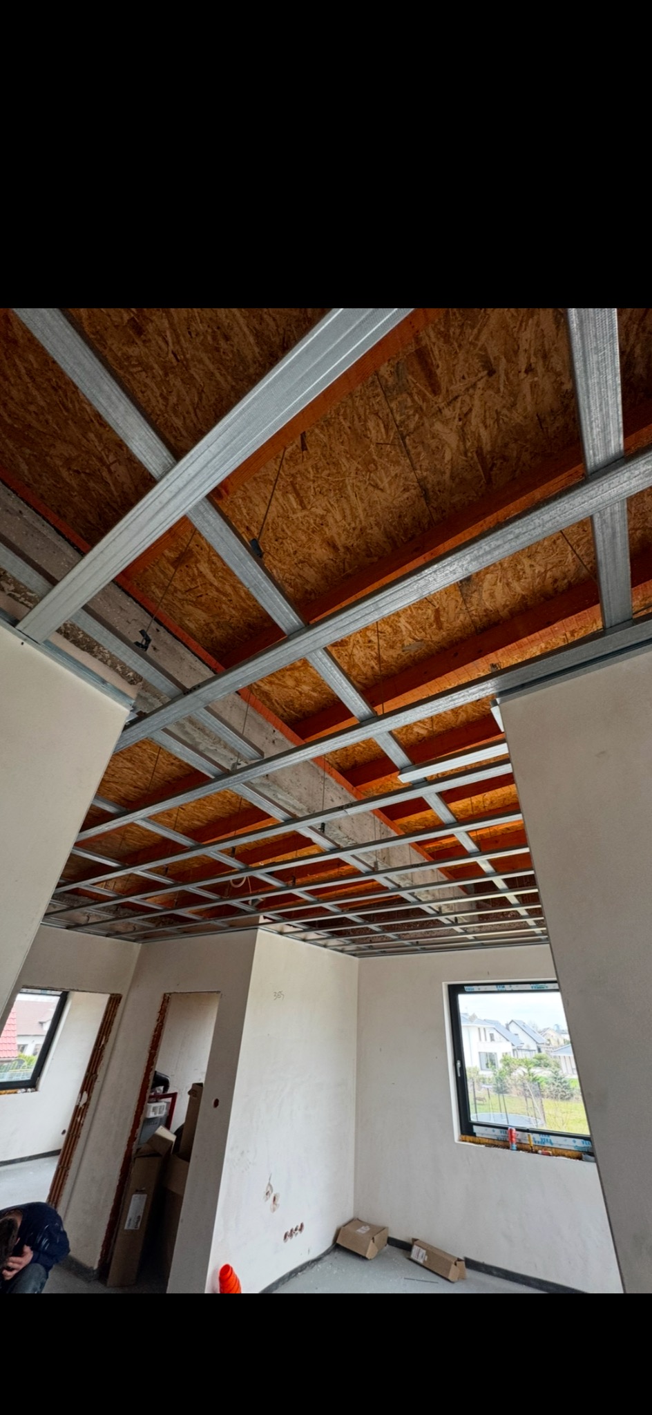 Montaż stelaża sufitu podwieszanego z płyt karton-gips, widok na drewniane elementy konstrukcyjne. W tle okno i fragment ściany z instalacją elektryczną.