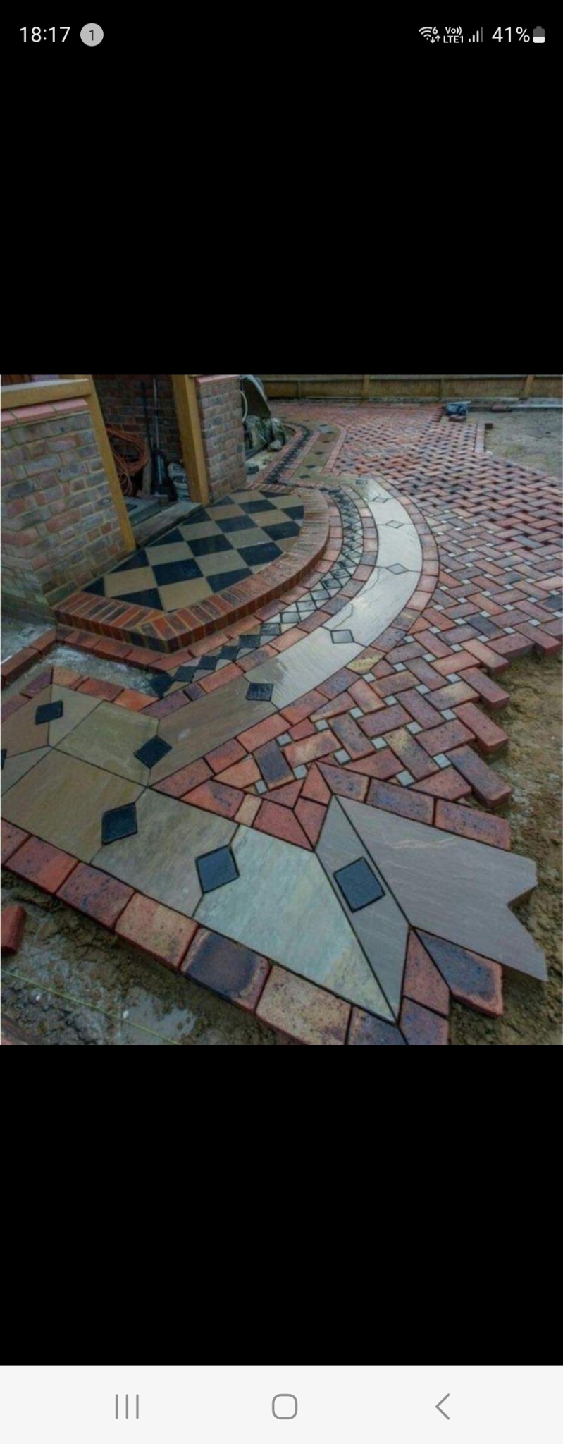 Układanie wzorzystej nawierzchni z cegły i kamienia w ogrodzie, widoczny fragment schodów z szachownicą.