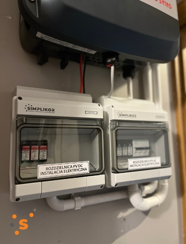 Dwa rozdzielnice elektryczne Simplikor zamontowane na ścianie, z etykietami 'Rozdzielnica PV DC Instalacja Elektryczna' oraz 'Rozdzielnica PV AC Instalacja Elektryczna', podłączone do falownika SYMO.