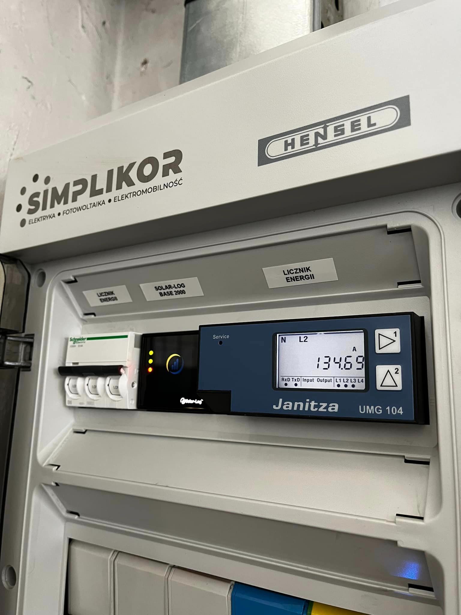 Rozdzielnica elektryczna Hensel z zainstalowanym licznikiem energii Janitza UMG 104 oraz zabezpieczeniami Schneider Electric, z widocznym logo firmy Simplikor, specjalizującej się w elektryce...