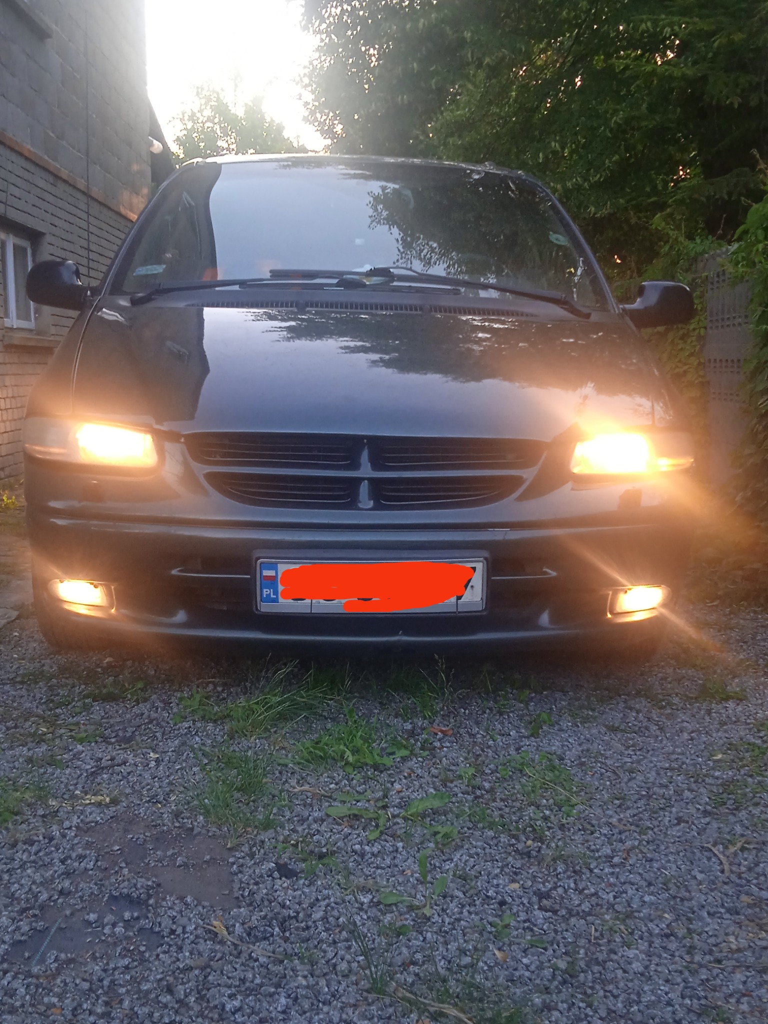 Przód ciemnego busa z włączonymi światłami, zaparkowanego na żwirowym podjeździe w Częstochowie, z widoczną polską tablicą rejestracyjną.