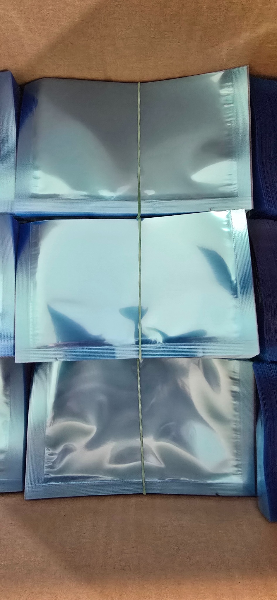 Ułożone w stos paczki w błyszczących, błękitnych foliowych opakowaniach, związane cienkim, zielonym sznurkiem.