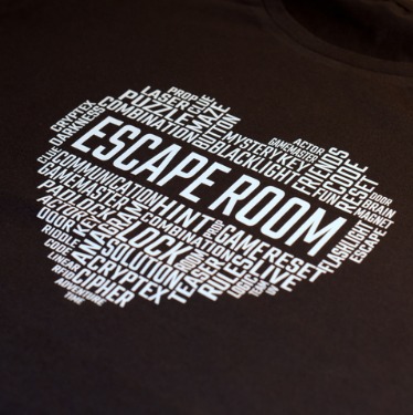 Ciemna koszulka z białym nadrukiem w kształcie serca, wypełnionego słowami związanymi z escape roomami, takimi jak 'ESCAPE ROOM', 'PUZZLE', 'LOCK', 'COMBINATION', 'CLUE' i inne.
