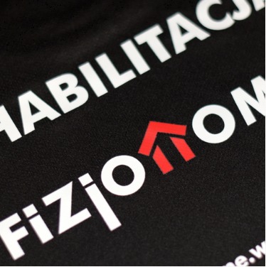 Czarna koszulka z białym napisem 'REHABILITACJA' i 'FIZJO' oraz czerwonym logo strzałki skierowanej w górę.