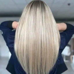 Długie, proste, blond włosy z ciemniejszym odrostem, ułożone na plecach, widok z tyłu, kobieta w granatowej bluzie.