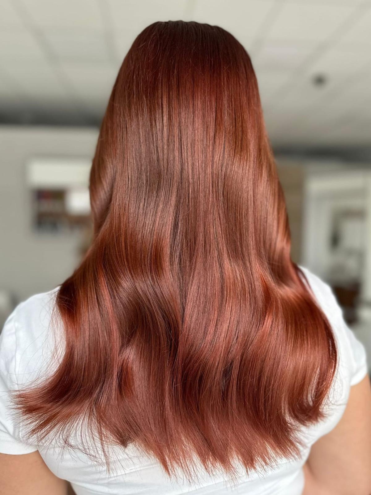 Długie, falowane włosy w odcieniach miedzianej czerwieni, widok z tyłu, z delikatnym połyskiem.