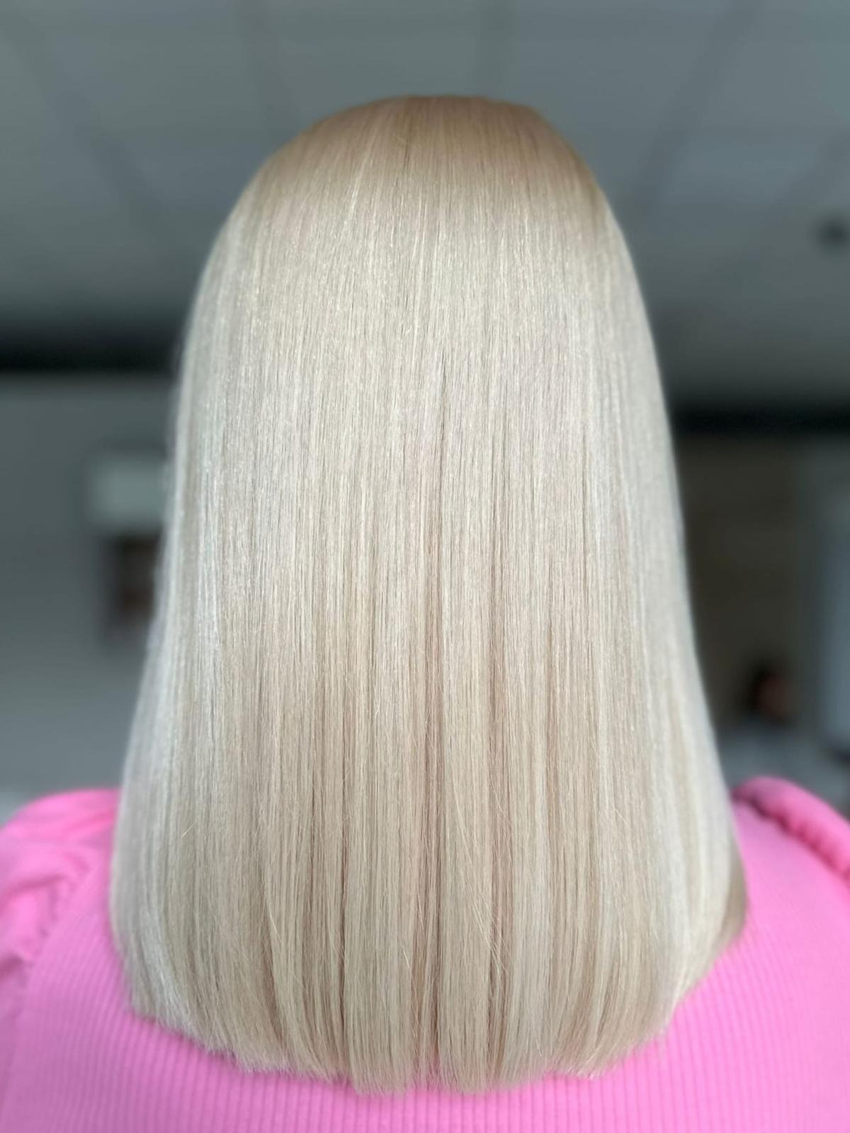Tył głowy z idealnie prostymi, platynowymi włosami o długości do ramion, końcówki delikatnie podwinięte do środka, ubrana w różową bluzkę.